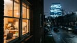 Nachts von der Straße aus: ein warm beleuchtetes Küchenfenster mit Geschirrständer und Kinderbecher, dahinter ein Bürohochhaus mit brennenden Stockwerken