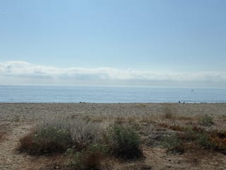 Im Himmel leichte Wolken, die Sonne hoch über dem Meer.