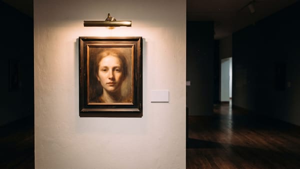 Gemaltes Porträt in einem dunklen Rahmen an einer Galeriewand, warm von einer Bilderleuchte beschienen, daneben ein leeres weißes Schild